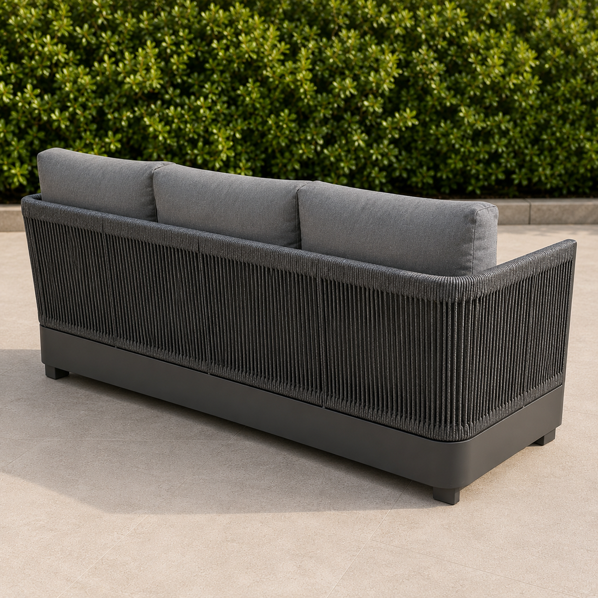 Dark grey woven rope backrest with light grey fabric cushions on stone tile floor outdoors.