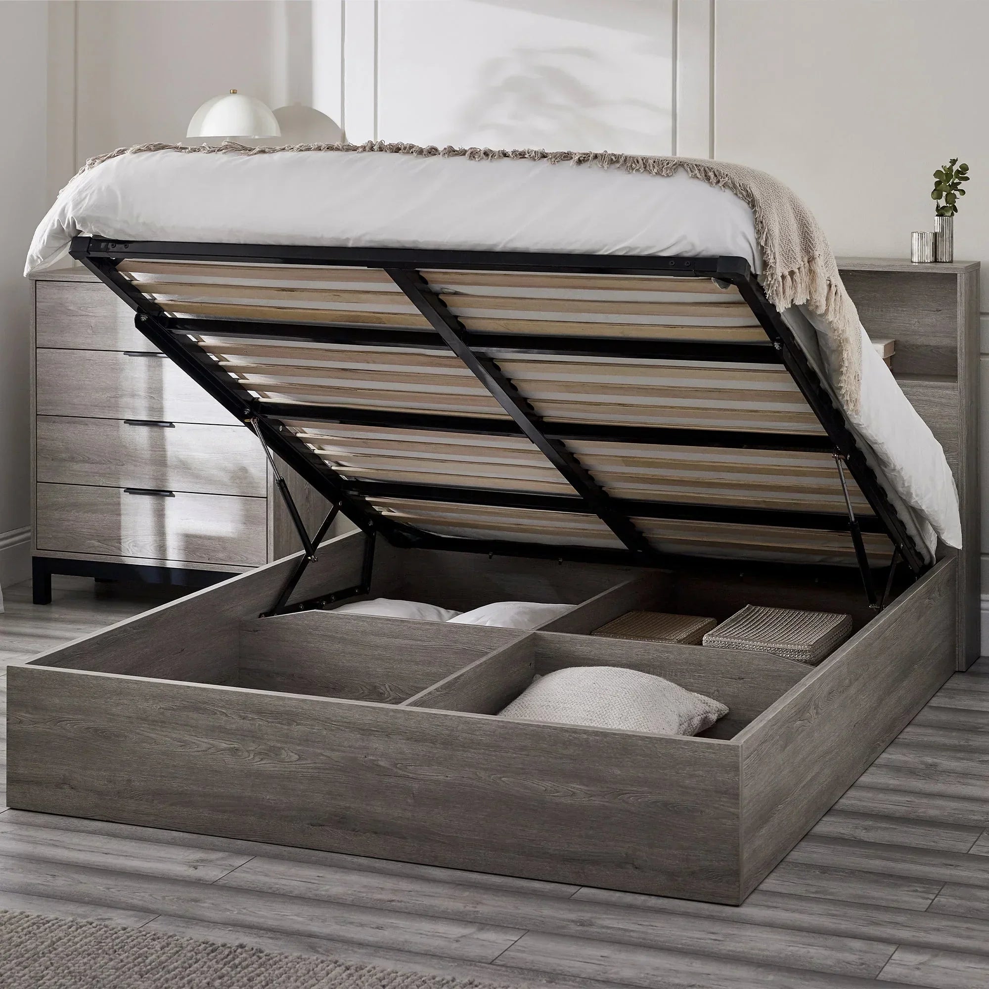 Grey oak ottoman bed with gas lift open, showing underbed storage compartments in bedroom