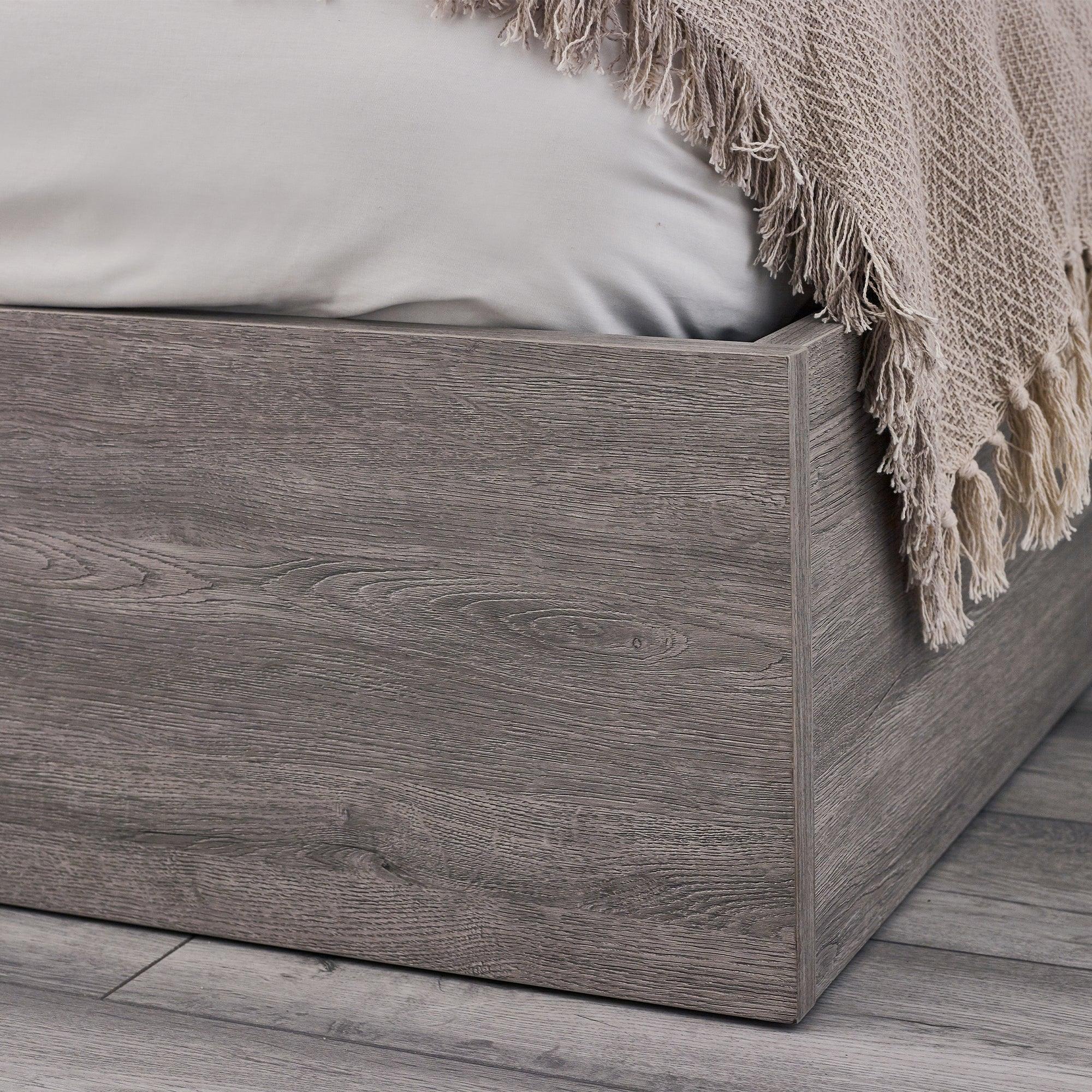 Grey oak ottoman storage bed corner with wood grain detail and fringe throw blanket
