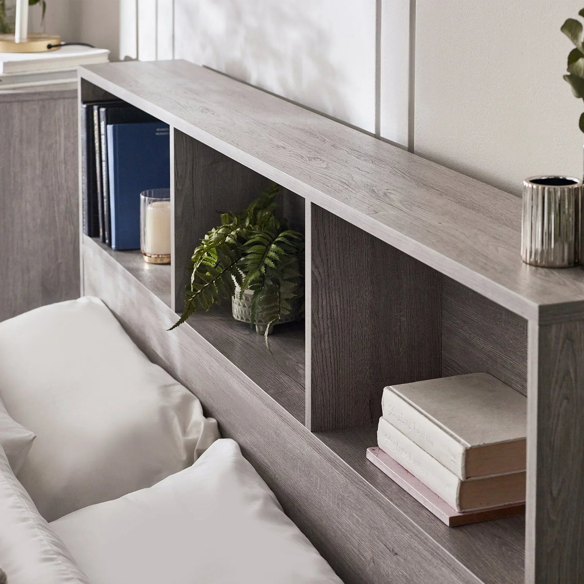 Grey oak ottoman storage bed headboard with shelf, books, plant, and candle detail