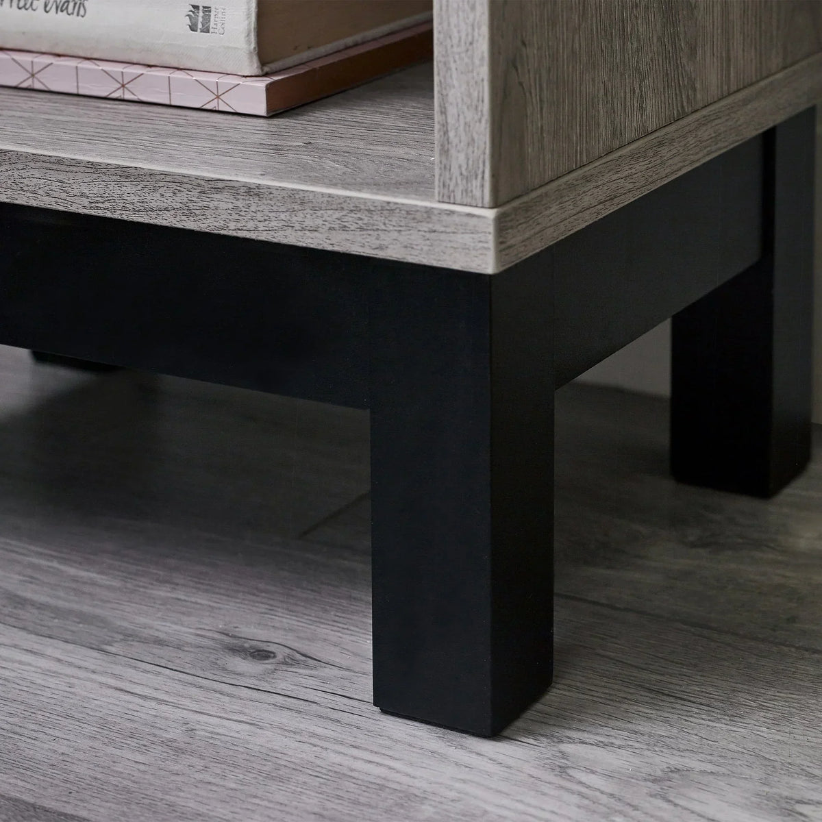 Grey oak bedside table corner with black legs and shelf holding books
