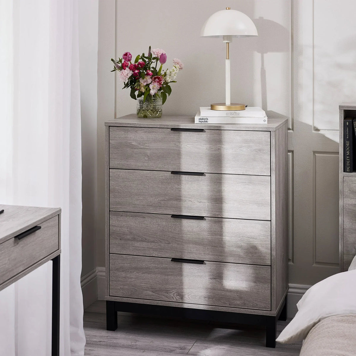 Grey oak 4 drawer chest with black handles in bedroom, topped with lamp and fresh flowers