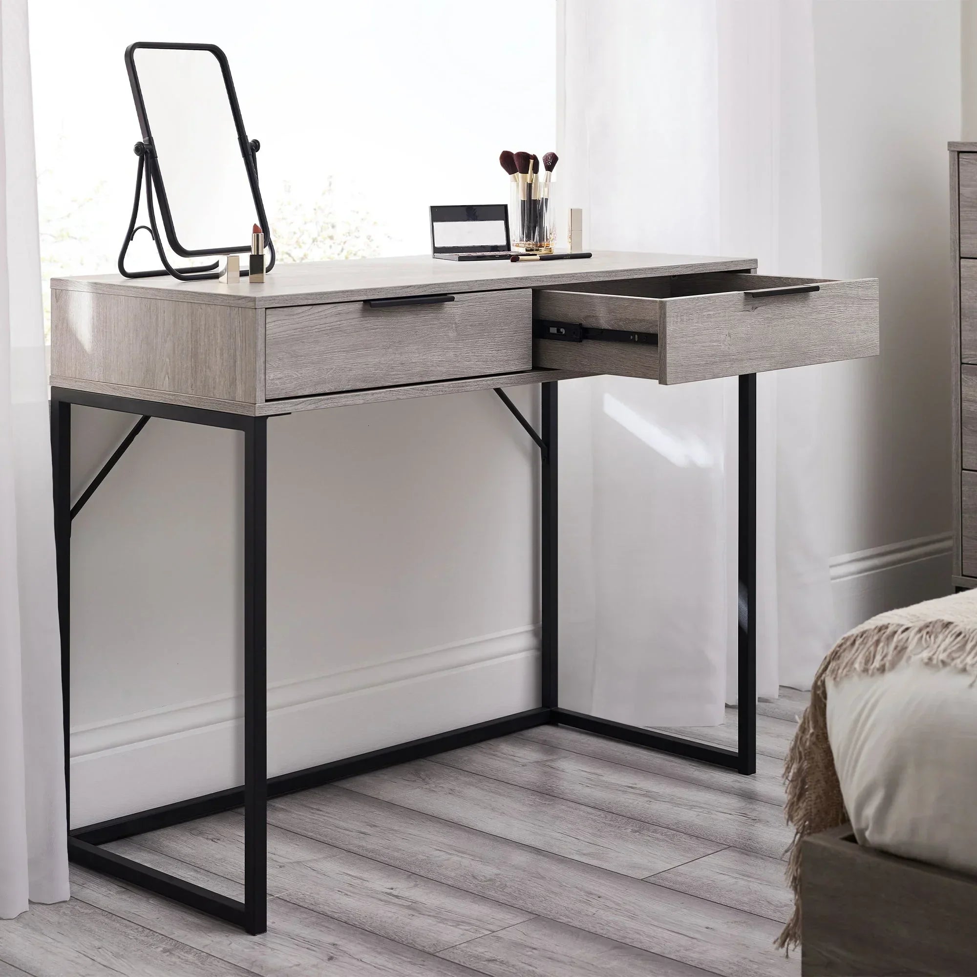 Grey oak two drawer dressing table with black metal legs, mirror, and makeup accessories