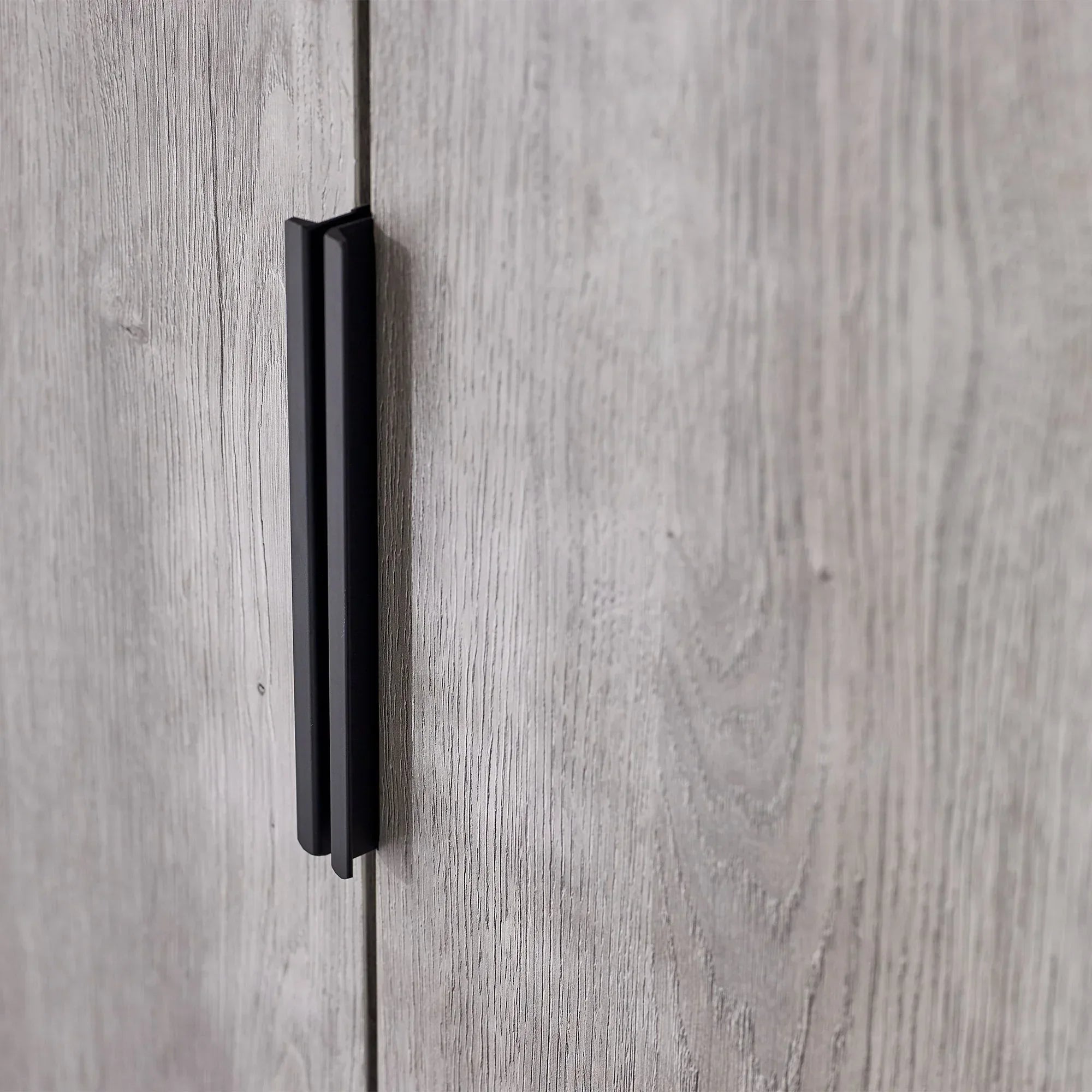 Black metal wardrobe handle on light oak wood grain door