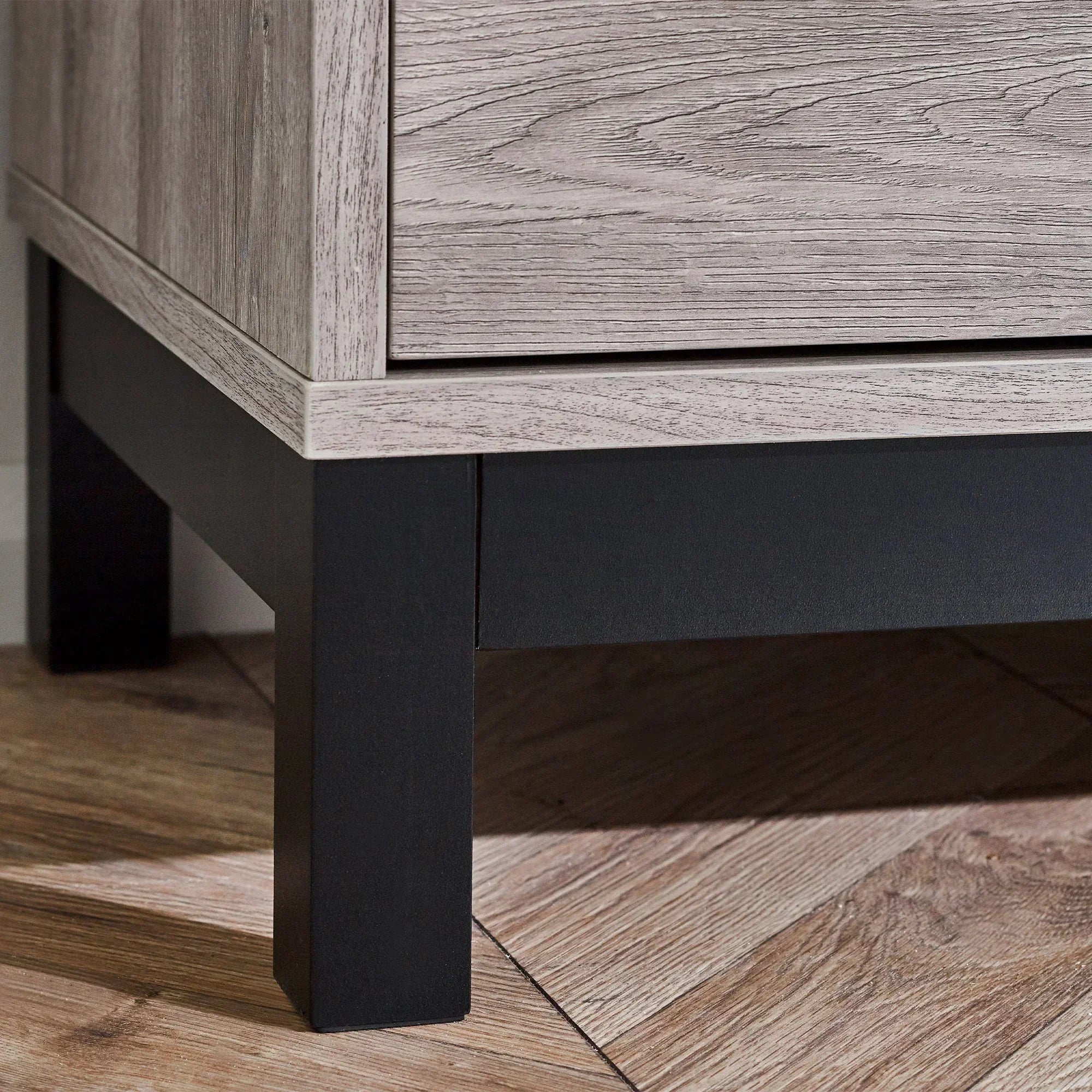 Grey oak TV unit detail showing wood grain finish and sturdy black legs on wooden flooring