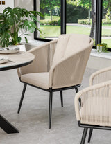 Beige rope dining chair with black legs beside modern round table in bright dining room