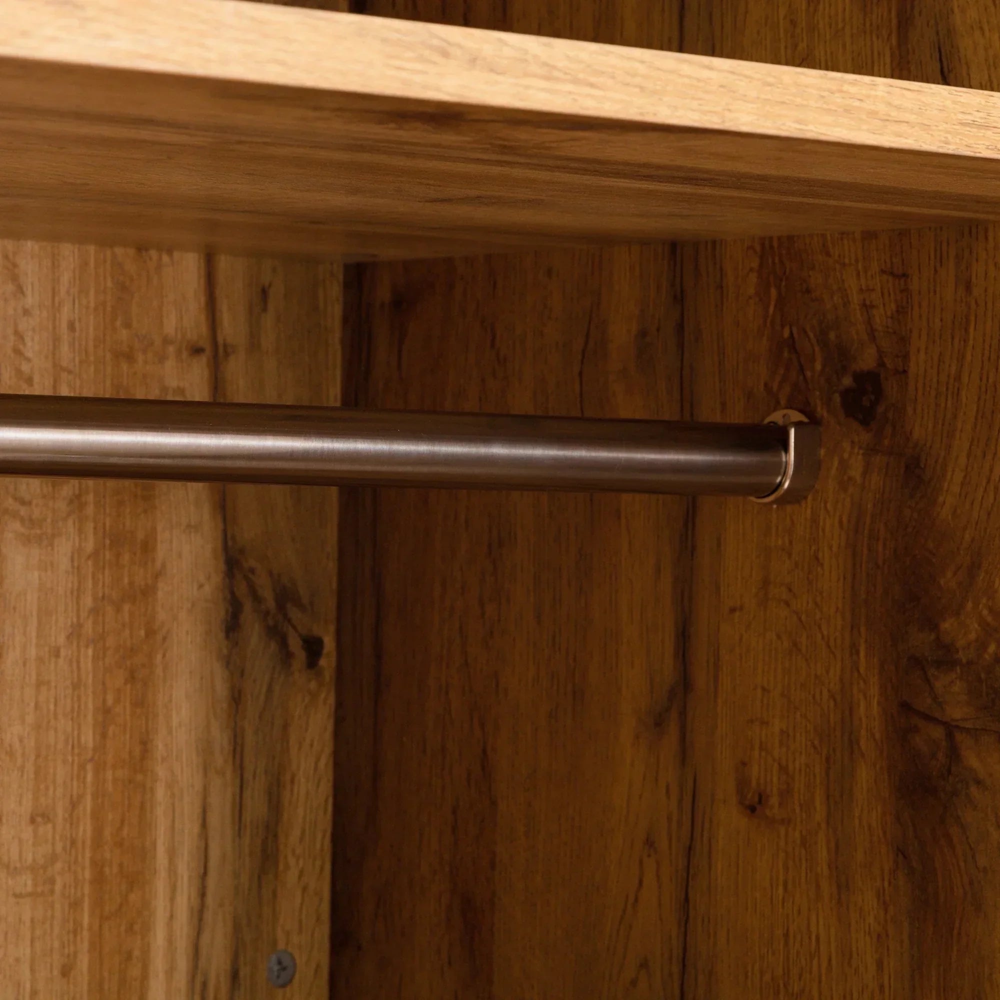 Closeup of wood wardrobe interior with metal hanging rail and top shelf