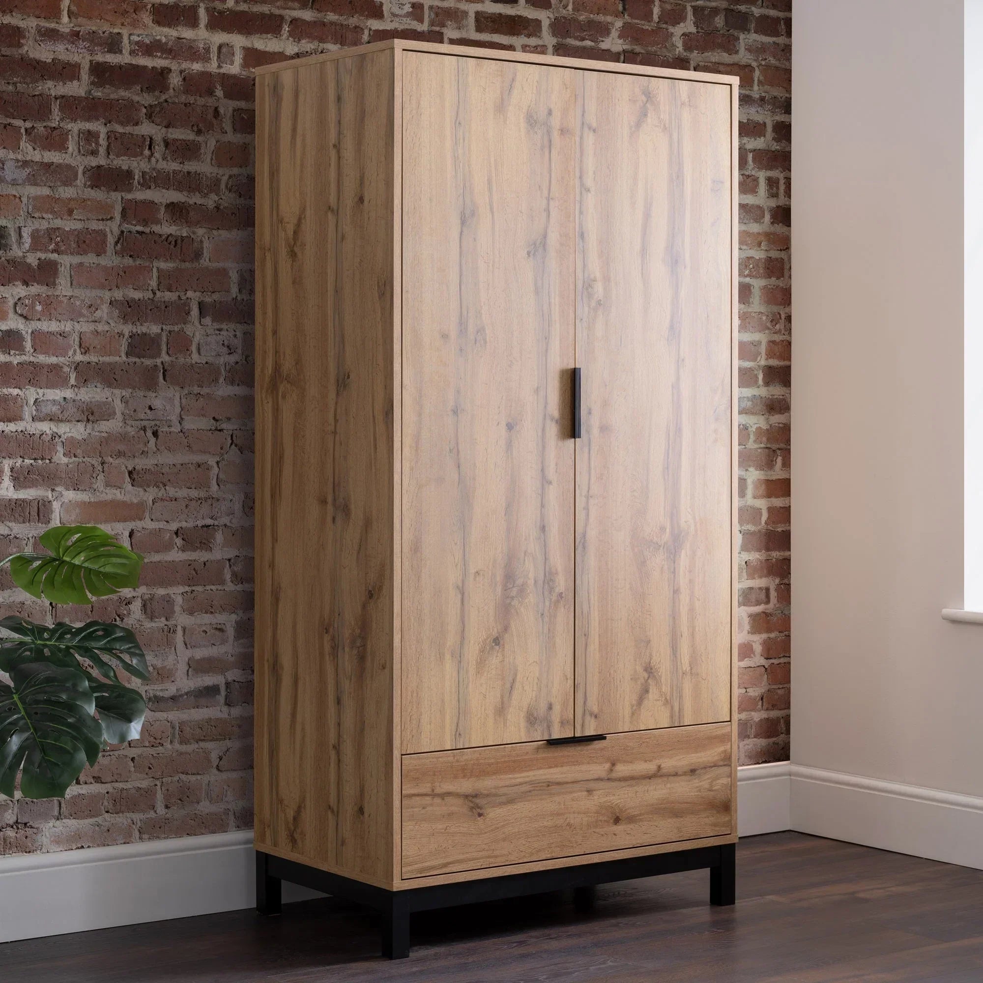Oak two door wardrobe with drawer and black handles against exposed brick wall