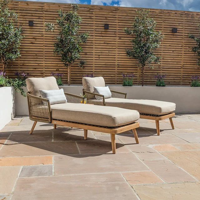 Pair of beige rattan garden loungers with cushions on stone patio with wooden privacy screen