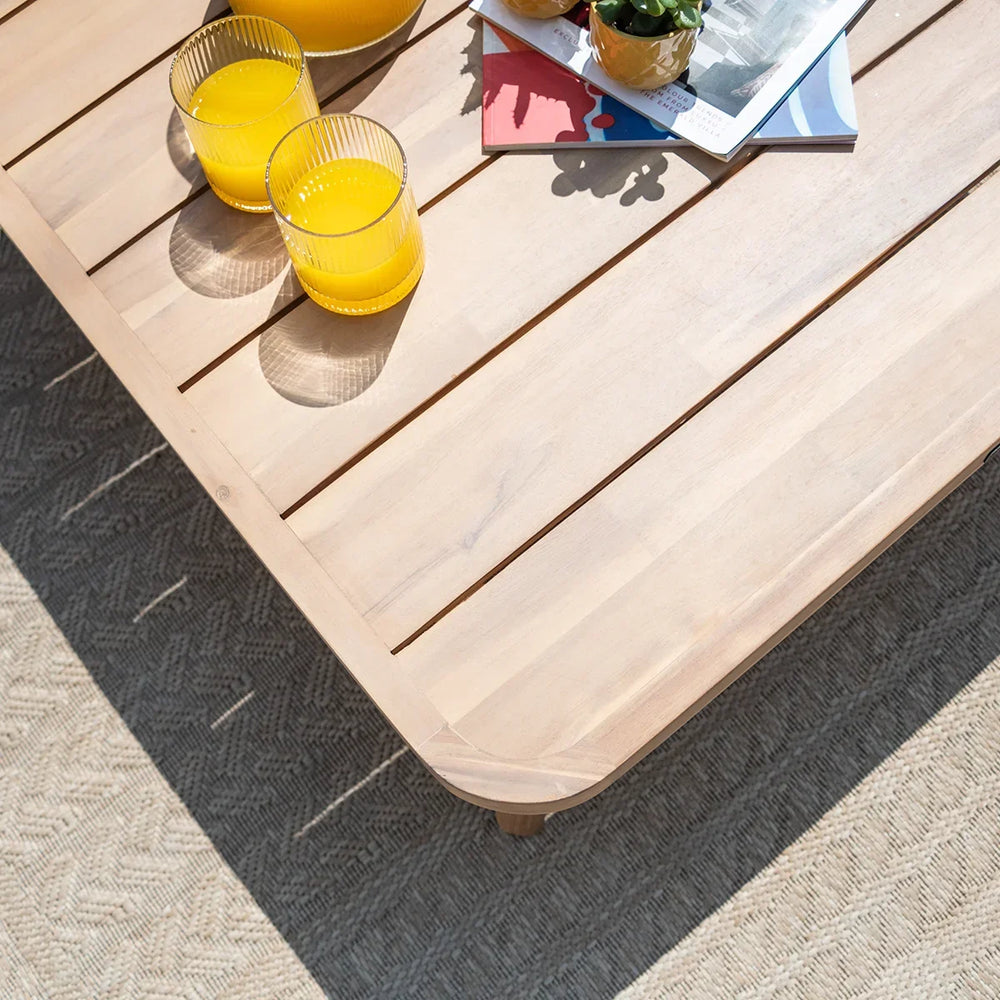 Light wood outdoor coffee table with drinks and magazines on textured patio rug