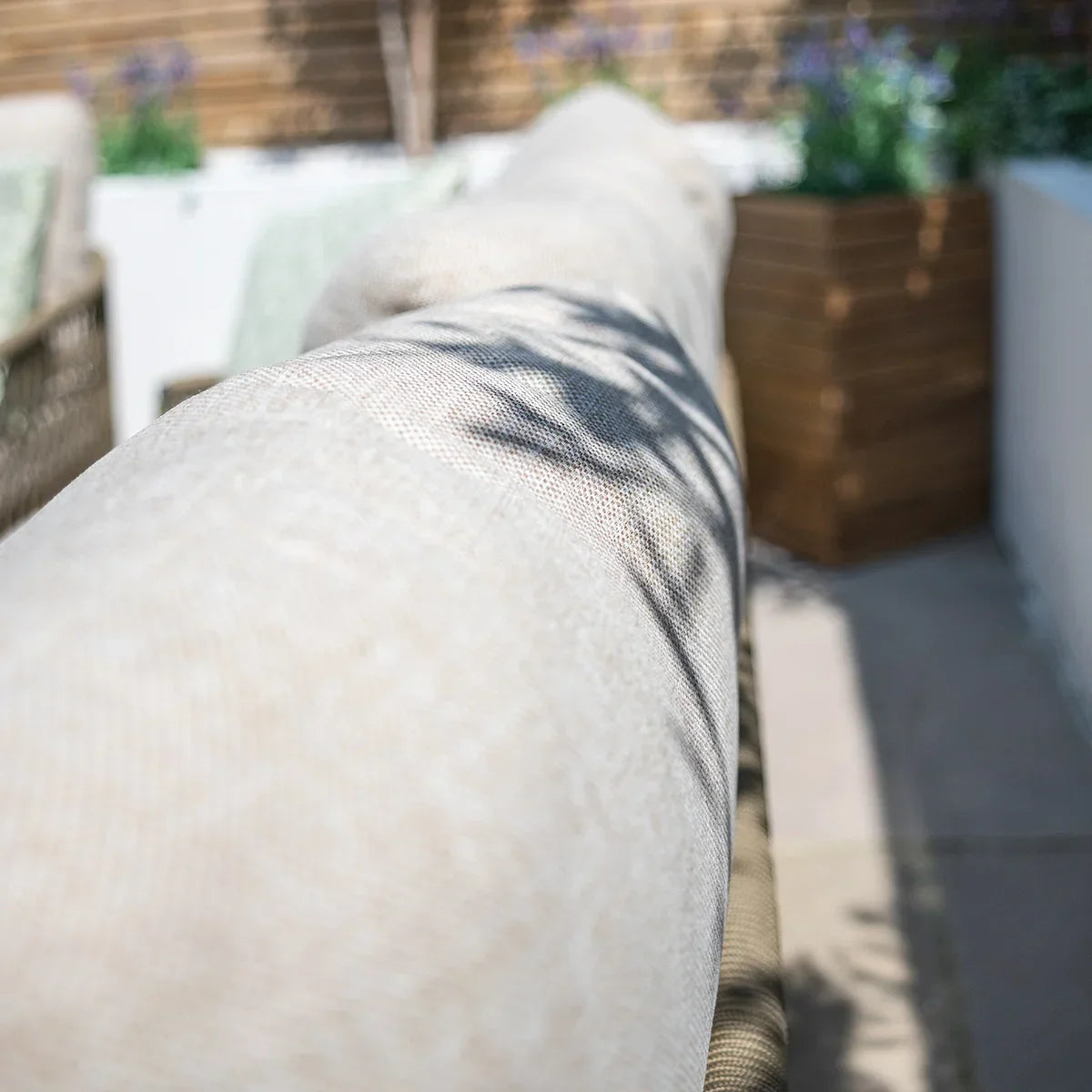 Close up of beige outdoor sofa backrest with textured fabric and patio planter in background