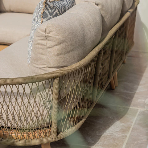 Outdoor rattan sofa with beige cushions and wooden legs on stone patio