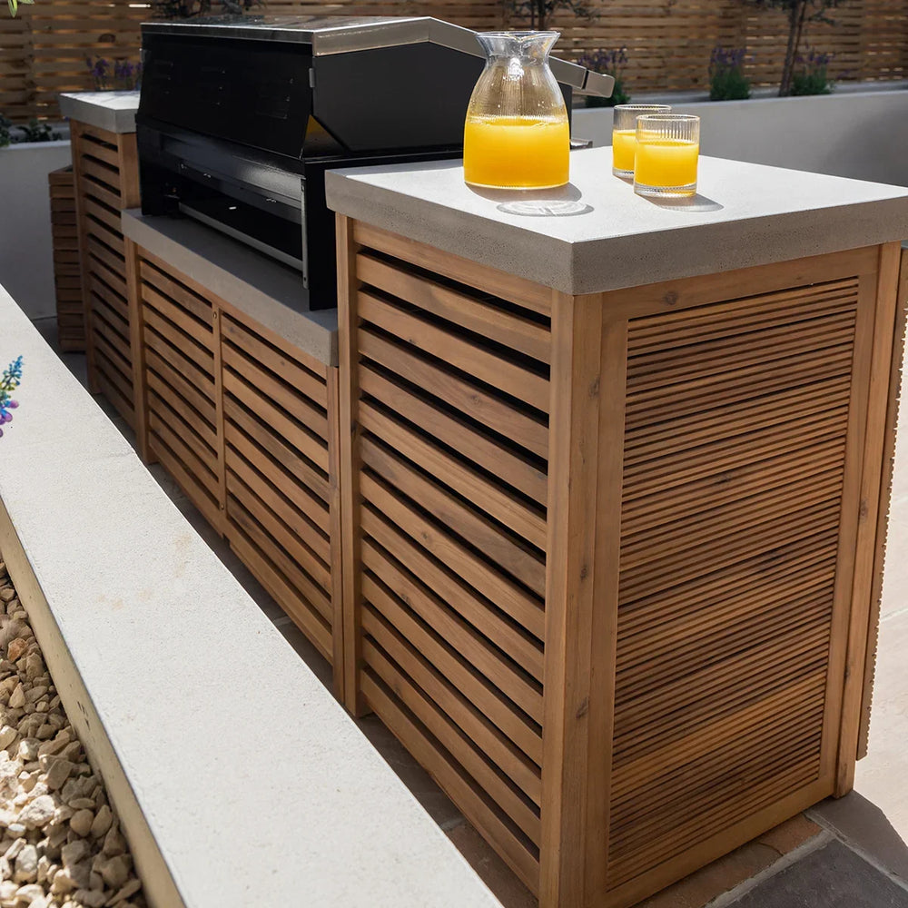 Outdoor kitchen island with wood slat cabinet, concrete countertop, and glass jug of juice