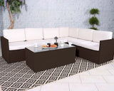 Brown rattan corner sofa set with cream cushions and glass coffee table on patterned rug