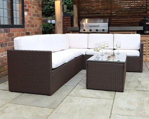 Brown rattan outdoor corner sofa set with cream cushions and glass coffee table on patio