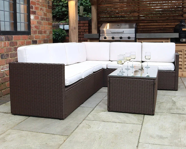 Brown rattan outdoor corner sofa set with cream cushions and glass coffee table on patio