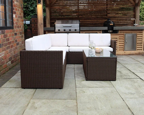 Brown rattan garden sofa set with white cushions and glass coffee table on patio