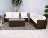 Brown rattan corner sofa set with white cushions and glass coffee table on patterned rug