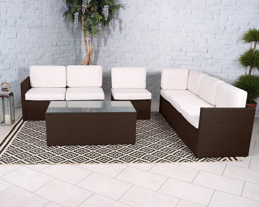 Brown rattan garden sofa set with cream cushions and glass coffee table on patterned rug