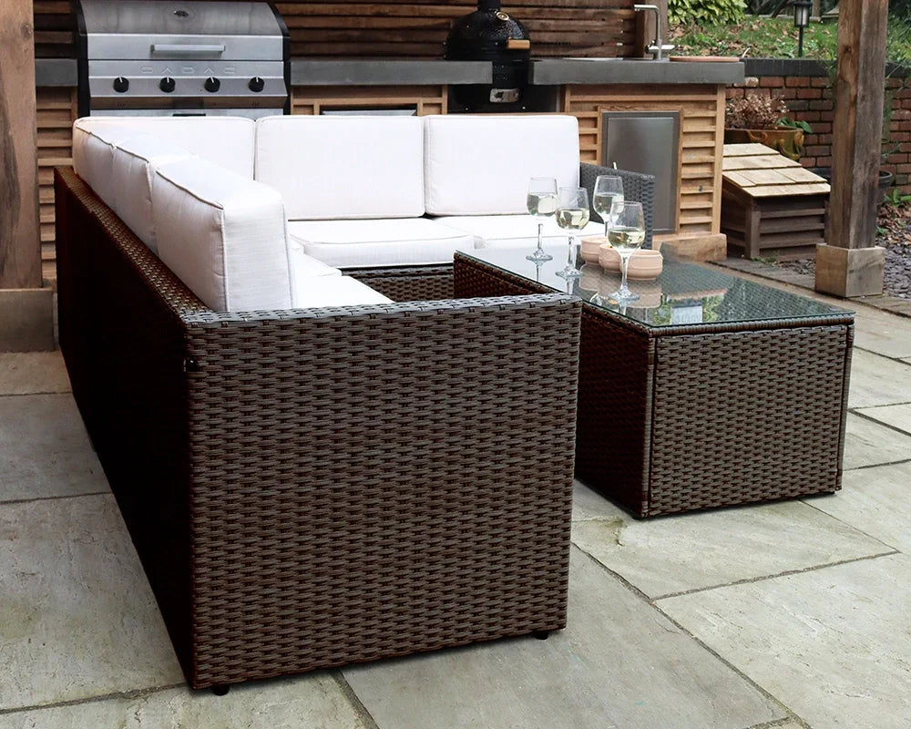 Brown rattan outdoor sofa set with white cushions and glass coffee table on patio