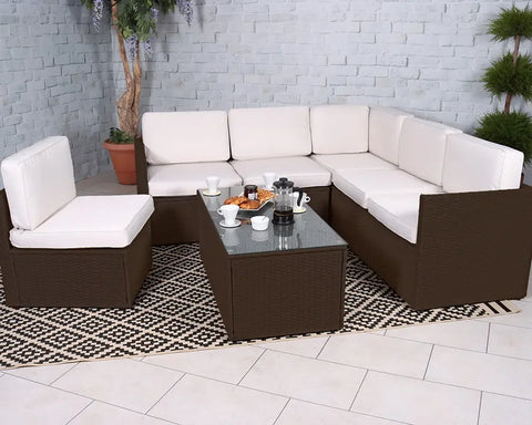 Brown rattan corner sofa set with cream cushions and glass top table on patterned rug