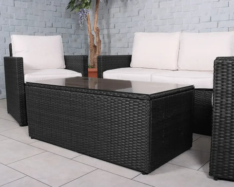 Black rattan garden furniture set with glass-top table and white cushions on patio tiles