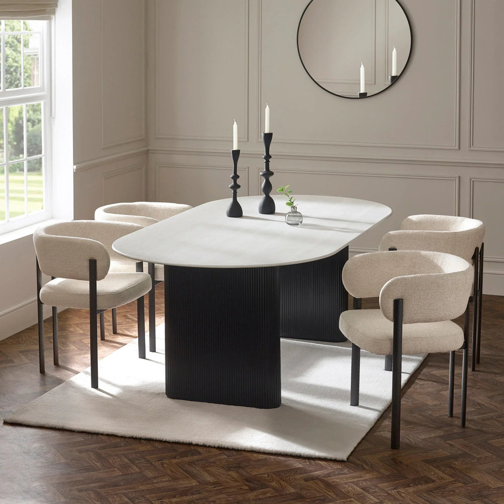 Modern dining table with oval white top and black base, surrounded by four beige chairs