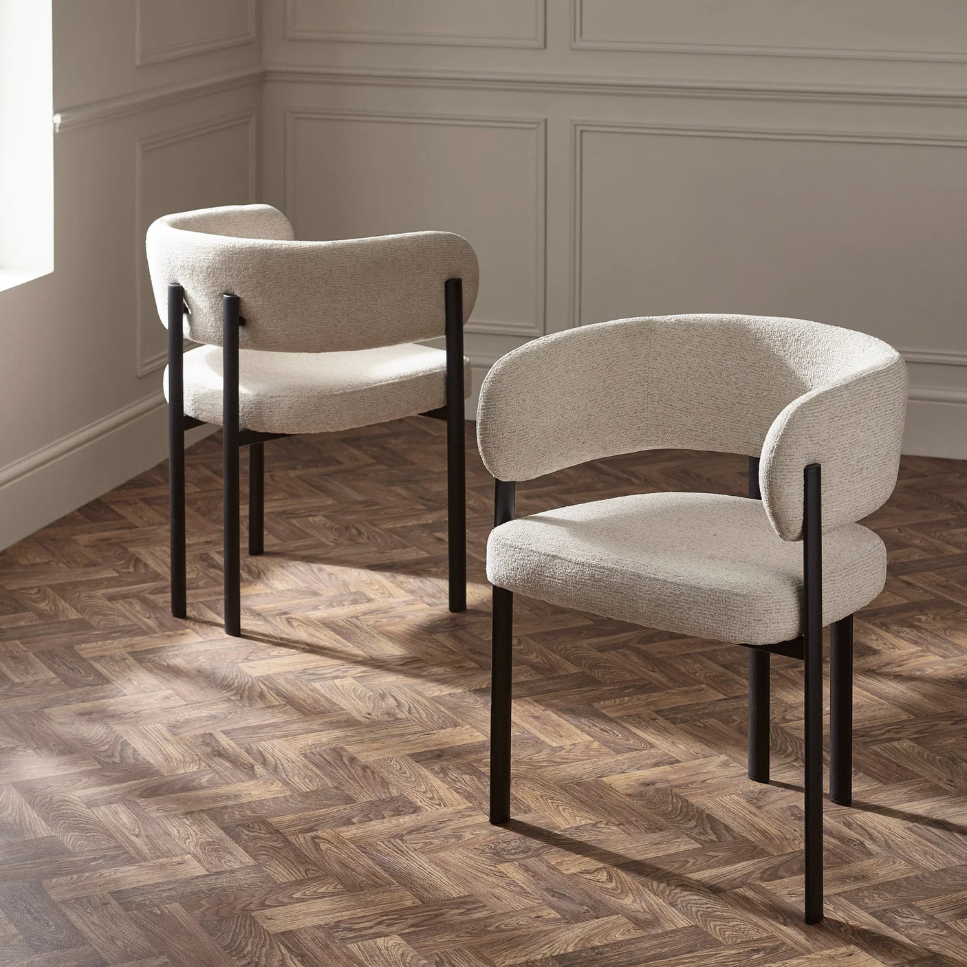 Pair of modern cream fabric dining chairs with curved backrest and black legs on wood floor