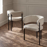 Pair of modern cream fabric dining chairs with curved backrest and black legs on wood floor