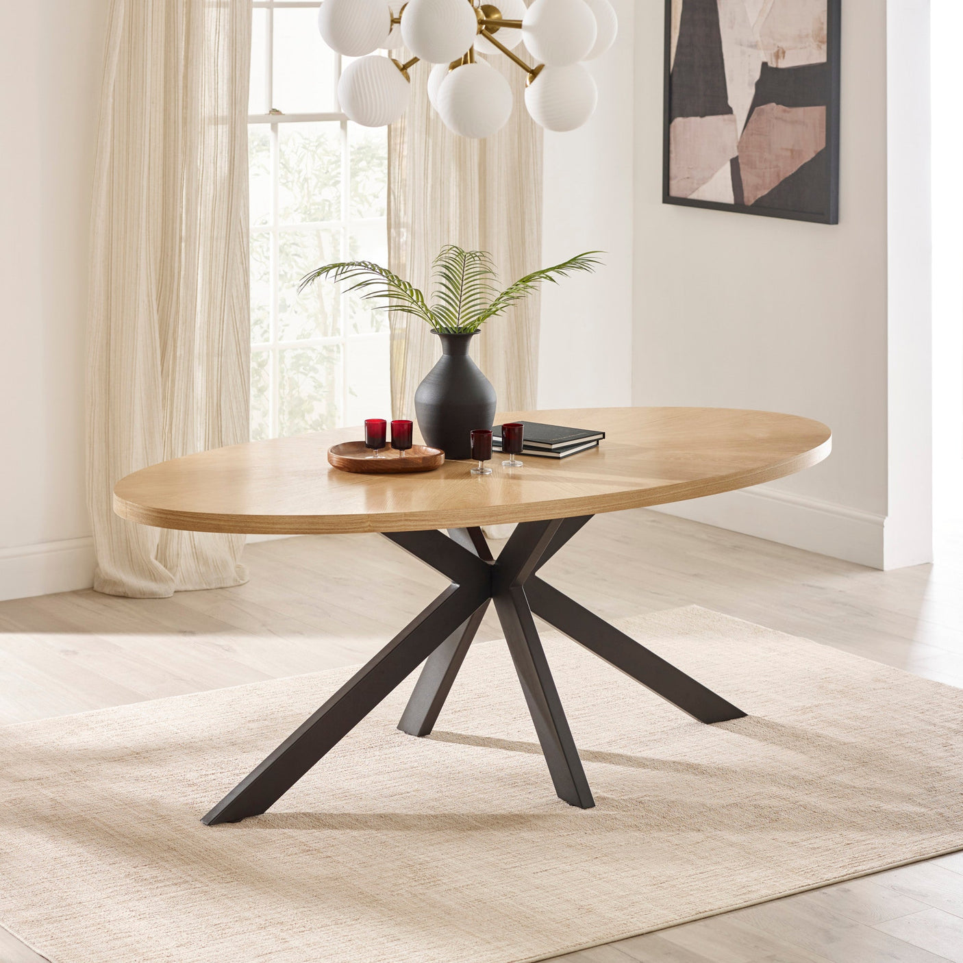 Oval dining table with light wooden top, black intersecting metal legs in bright room setting