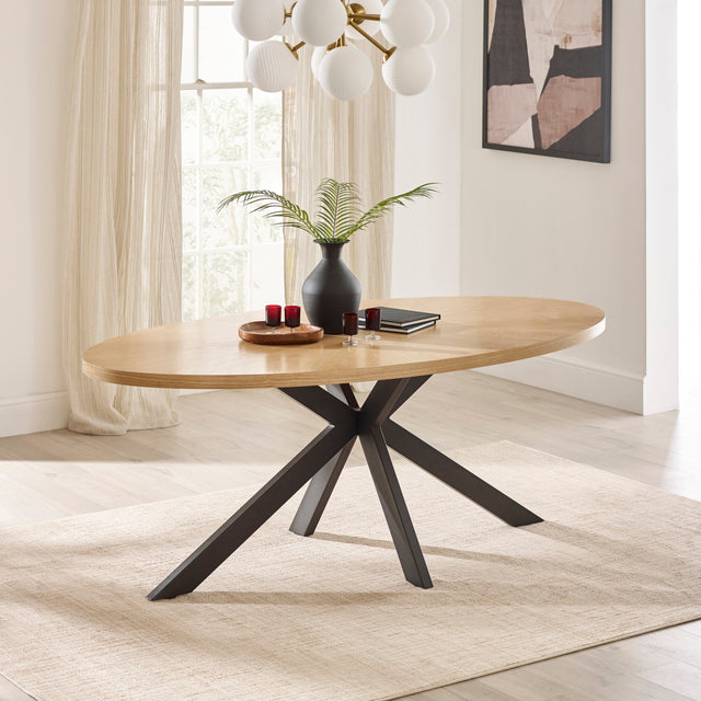 Oval dining table with light wooden top, black intersecting metal legs in bright room setting
