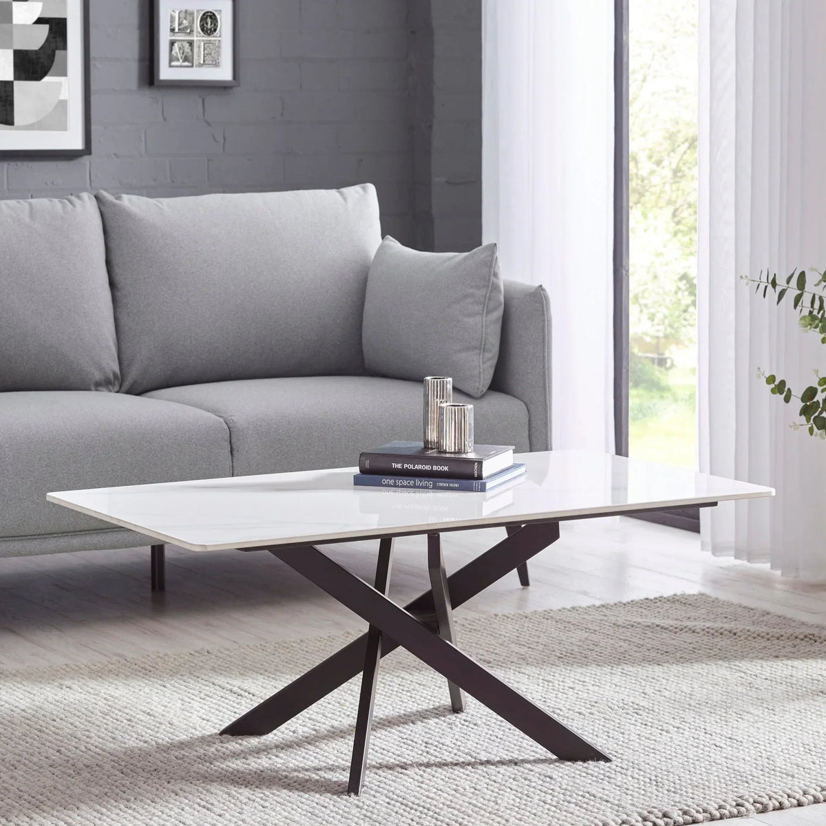 White marble coffee table with black crossed legs in modern living room next to grey sofa