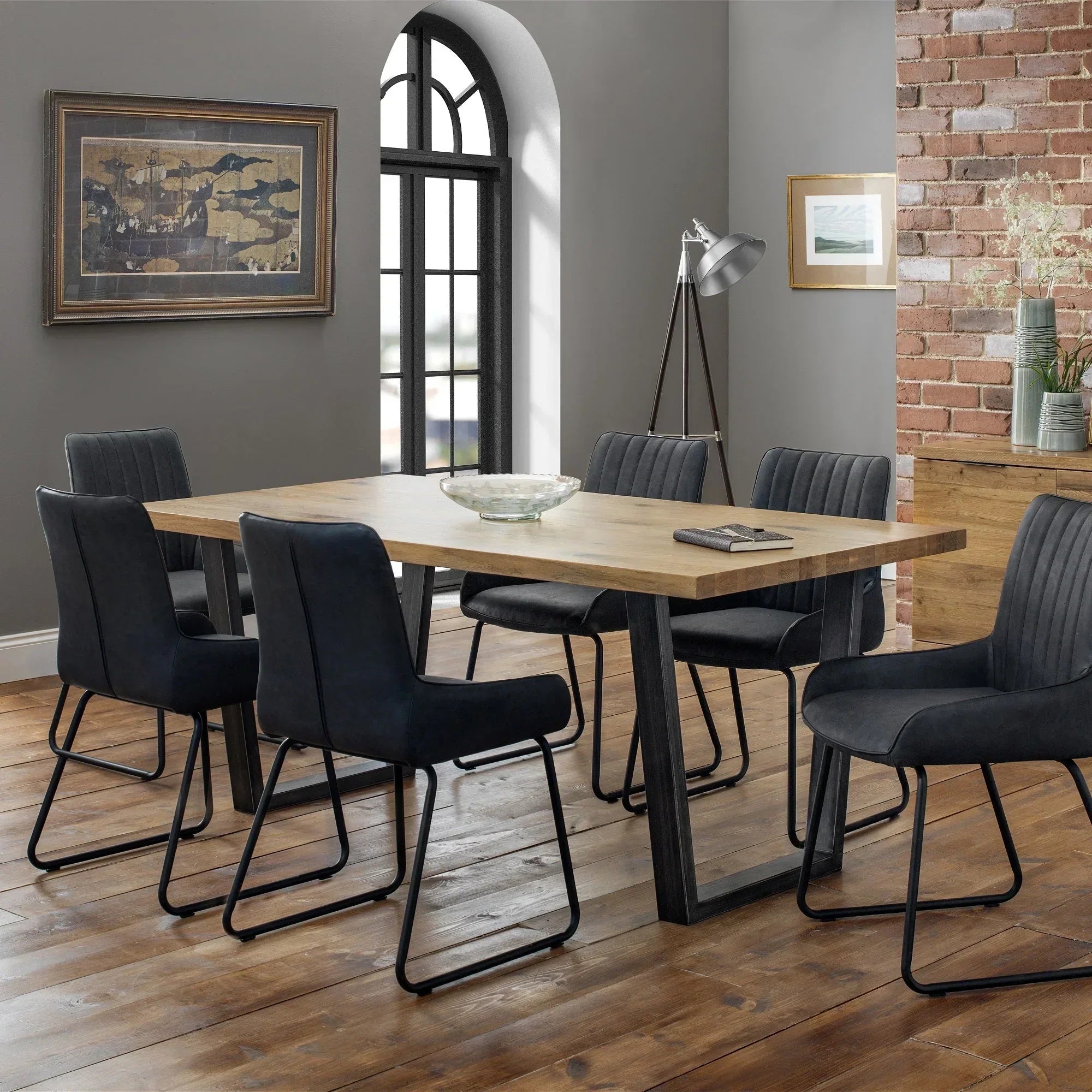 Oak dining table with black metal legs and six dark upholstered chairs in modern room