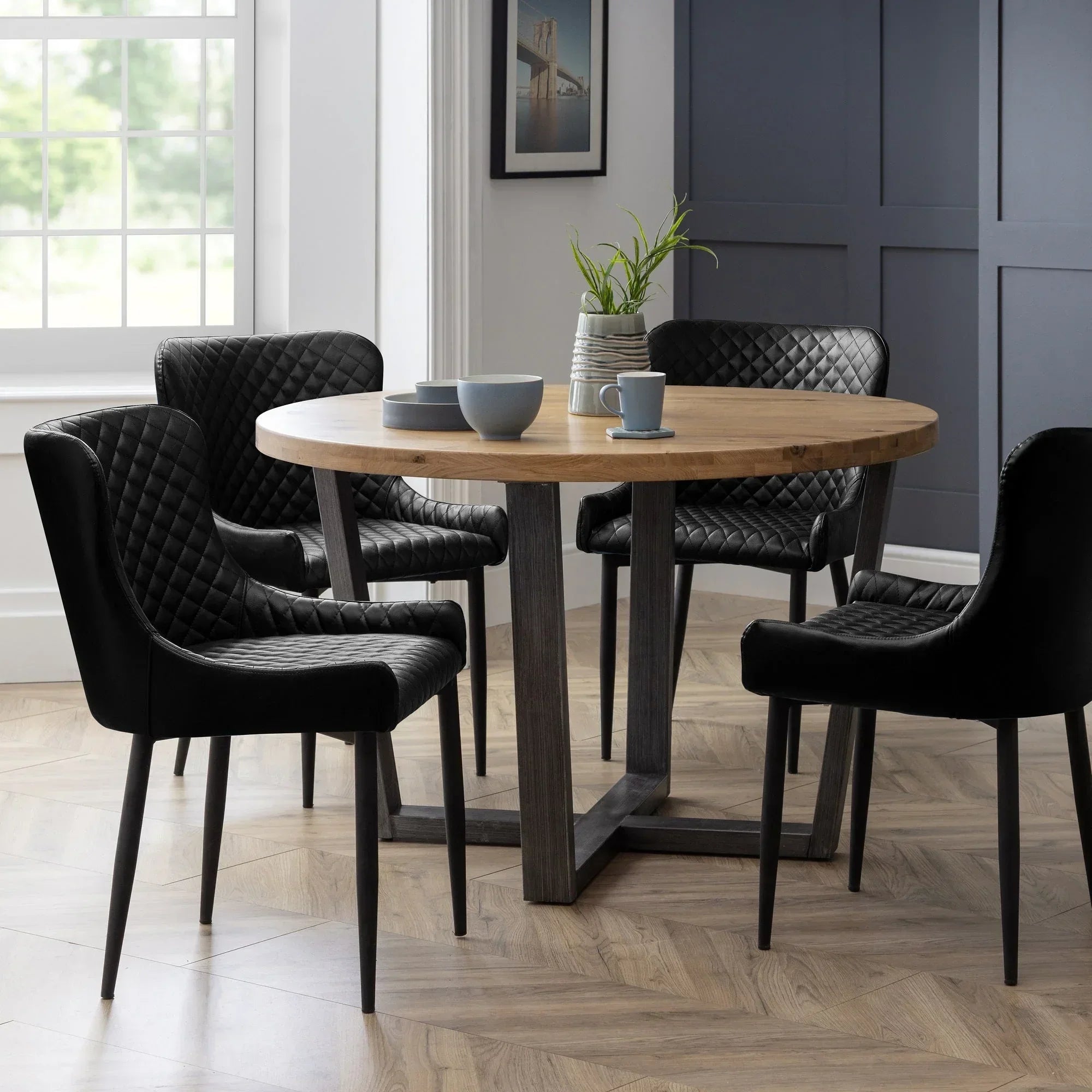 Round oak dining table with black quilted chairs in modern dining room