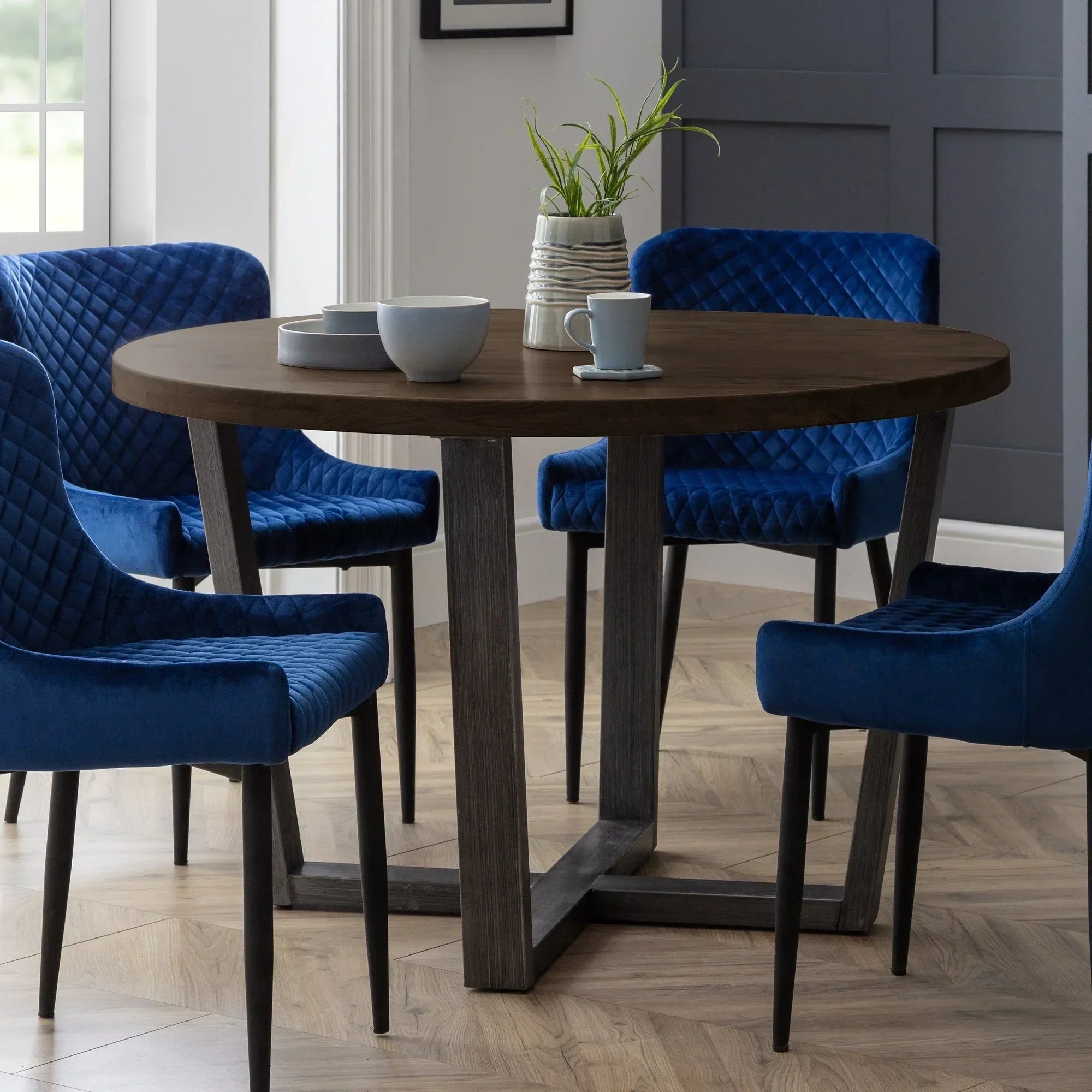 Round dark oak dining table with blue velvet chairs on wood floor