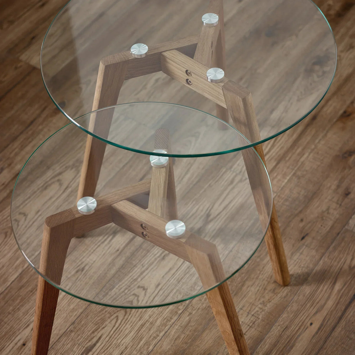 Round glass nest of tables with light wood frames on wooden floor, close-up detail