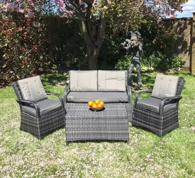 Grey rattan garden sofa set with coffee table and chairs on grass under blossoming tree