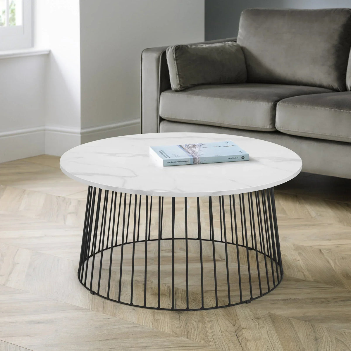 Round marble coffee table with black metal base in modern living room next to grey sofa