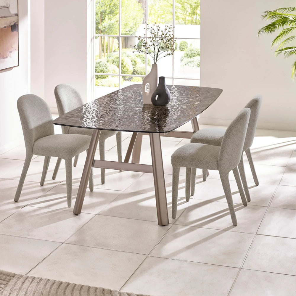 Glass top dining table with four grey upholstered chairs in bright modern dining room
