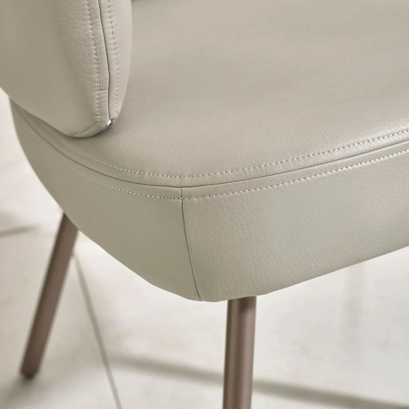 Close-up of beige faux leather dining chair seat with stitched detail and metal leg
