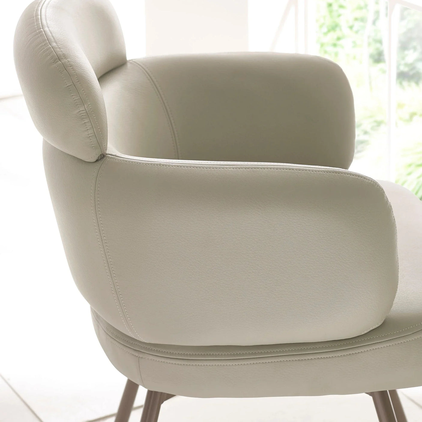 Beige leather accent chair with padded backrest and armrests, side view indoors