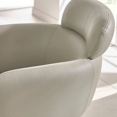 Light grey leather armchair with curved backrest and visible stitching in bright room