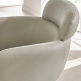 Light grey leather armchair with curved backrest and visible stitching in bright room
