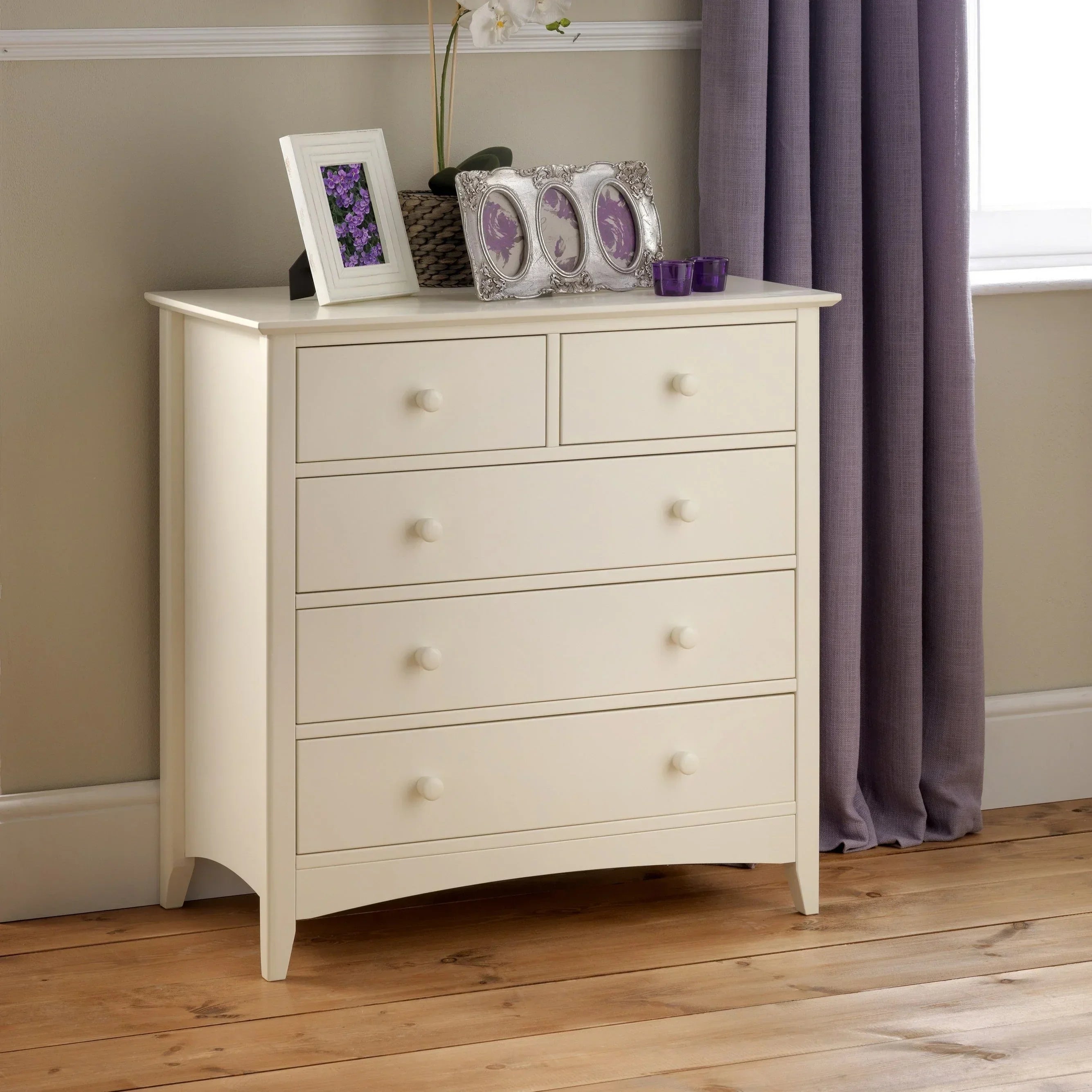 White chest of drawers with round knobs in a bedroom with wooden floor and purple curtains