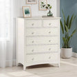 White chest of drawers with six knobs in bright bedroom corner next to window and plant