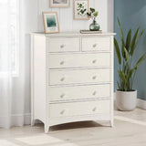 White chest of drawers with six knobs in bright bedroom corner next to window and plant