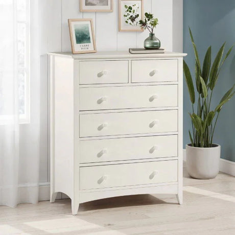 White chest of drawers with six knobs in bright bedroom corner next to window and plant