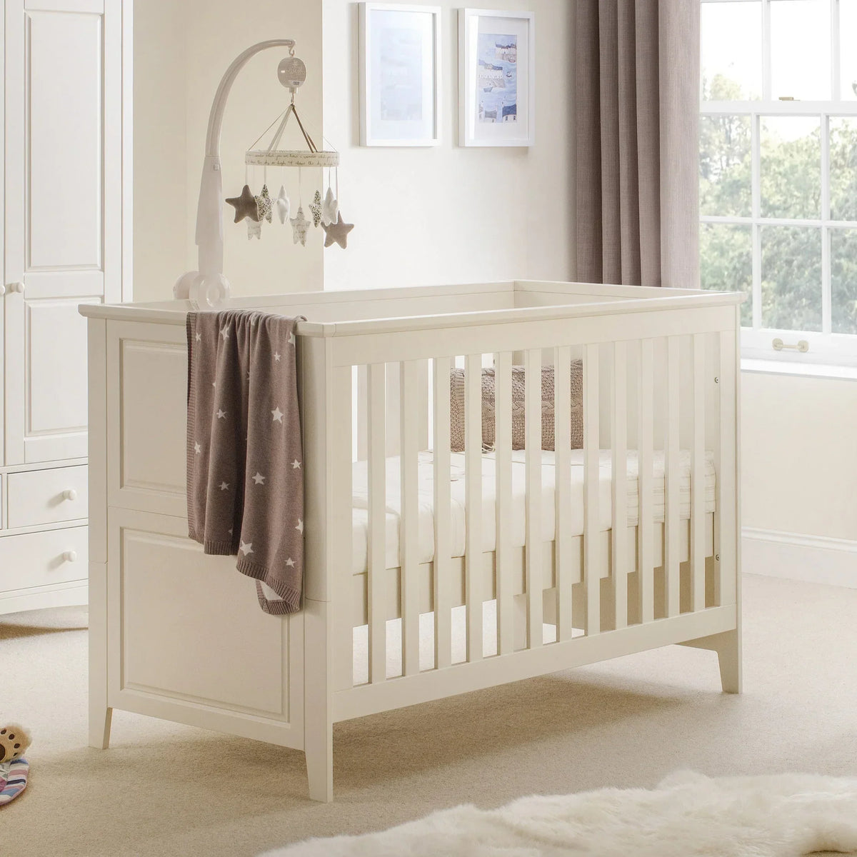White cot bed with slatted sides in neutral nursery, star blanket and hanging mobile