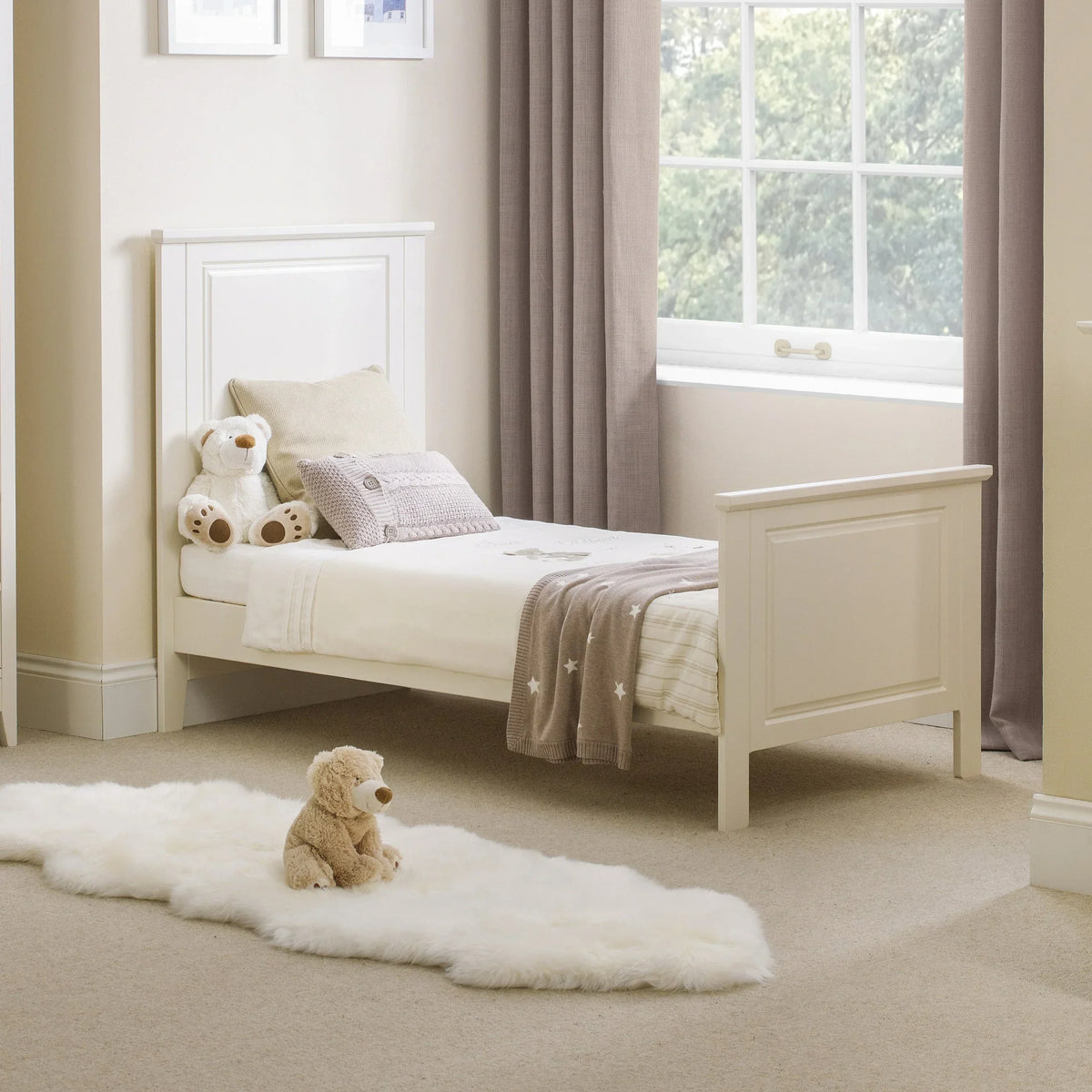 White wooden cot bed with beige bedding and teddy bears in a bright nursery room
