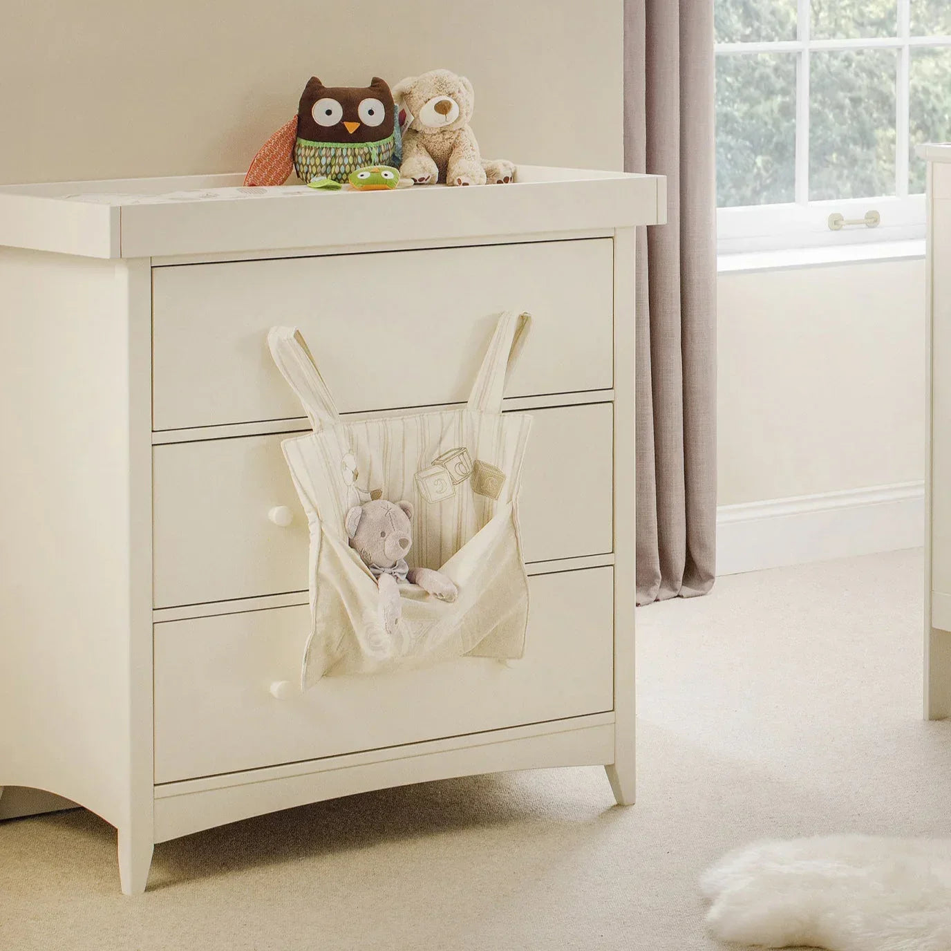 Cream changing station with drawers, soft toys on top, nursery storage pocket attached